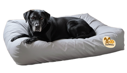 Black dog lies on a large, rectangular bolster dog bed covered with a light gray PawSheets dog bed cover 