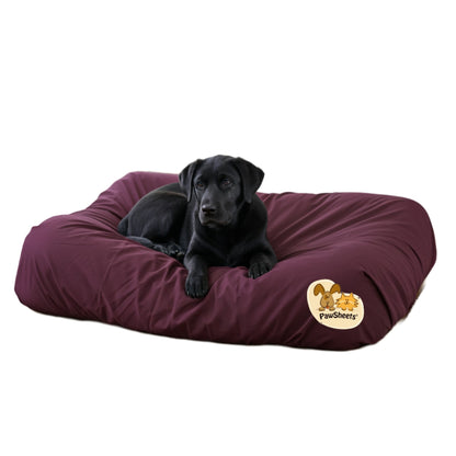 Black labrador retriever resting on a bolster style dog bed covered with a burgundy PawSheets dog bed cover
