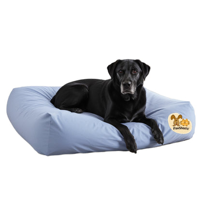 Black labrador retriever resting on a bolster style dog bed covered with a light blue PawSheets dog bed cover